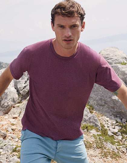 En mand iført en lilla Fruit of the Loom t-shirt og lyseblå shorts går blandt sten og klipper i et bjergrigt landskab.