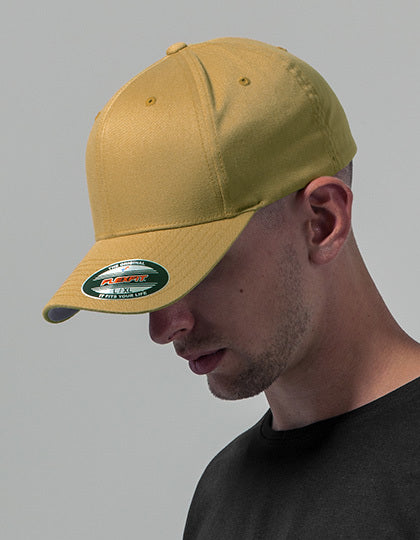 Manden bærer en gul kasket og kigger nedad. Han er iført en sort t-shirt i en neutral, ensfarvet baggrund. Kasketten har et mærkat på skyggen.